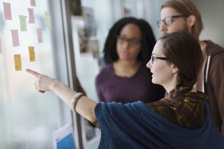 Creative colleagues reviewing ideas on wall in studio office.